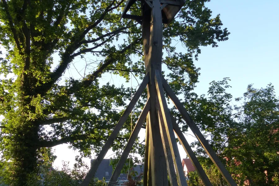Der hölzerne Varler Glockenstuhl mit seiner Glocke unter einem großen Baum