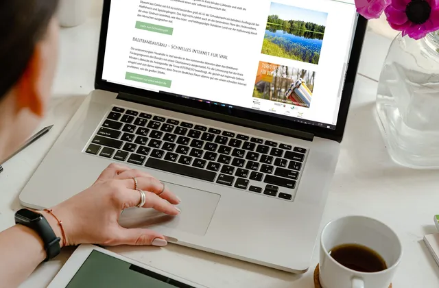 Eine Frau sitzt am Laptop und betrachtet die Website varl.de; daneben ein Tablet, eine Tasse Kaffee und Blumen