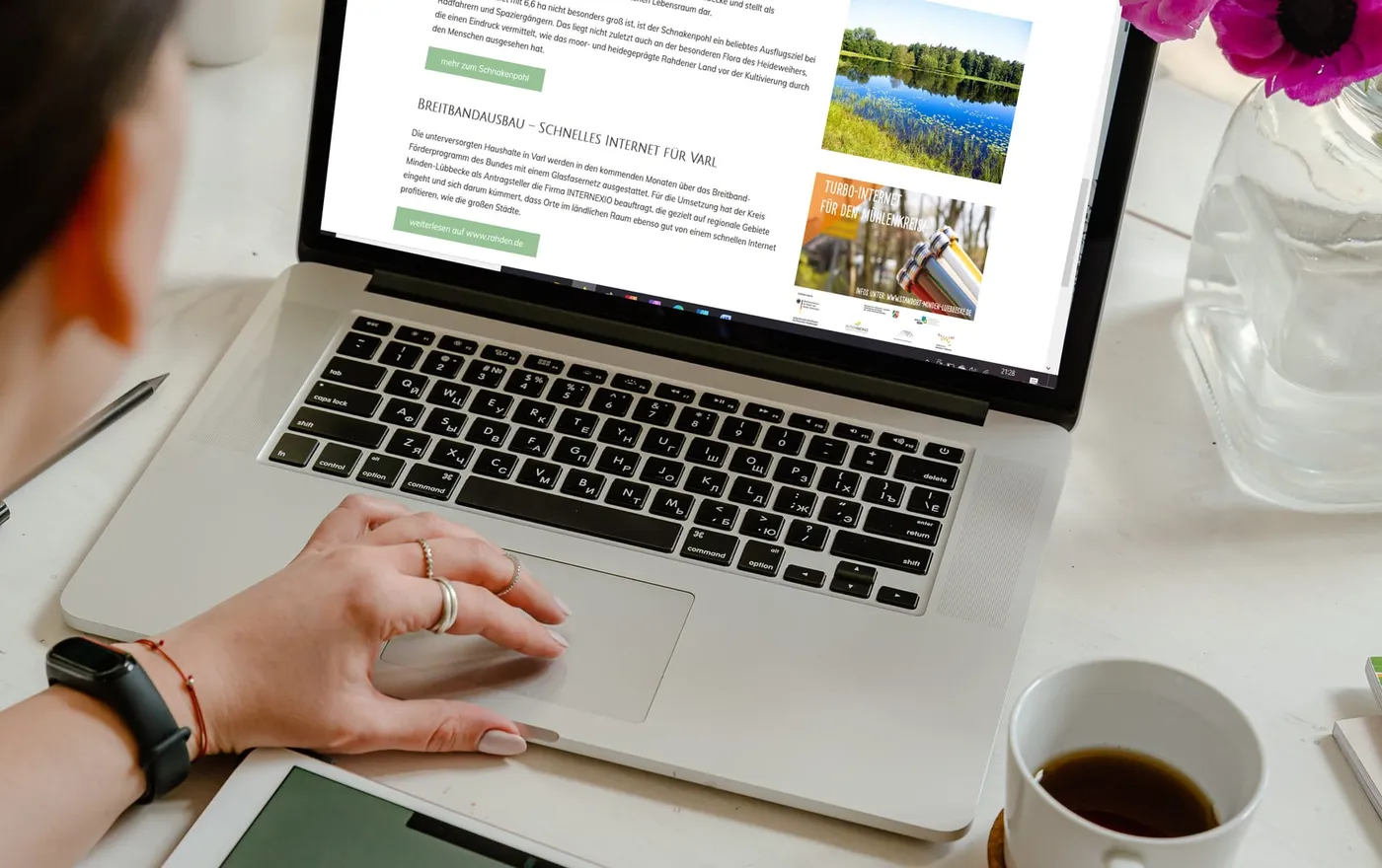 Eine Frau sitzt am Laptop und betrachtet die Website varl.de; daneben ein Tablet, eine Tasse Kaffee und Blumen