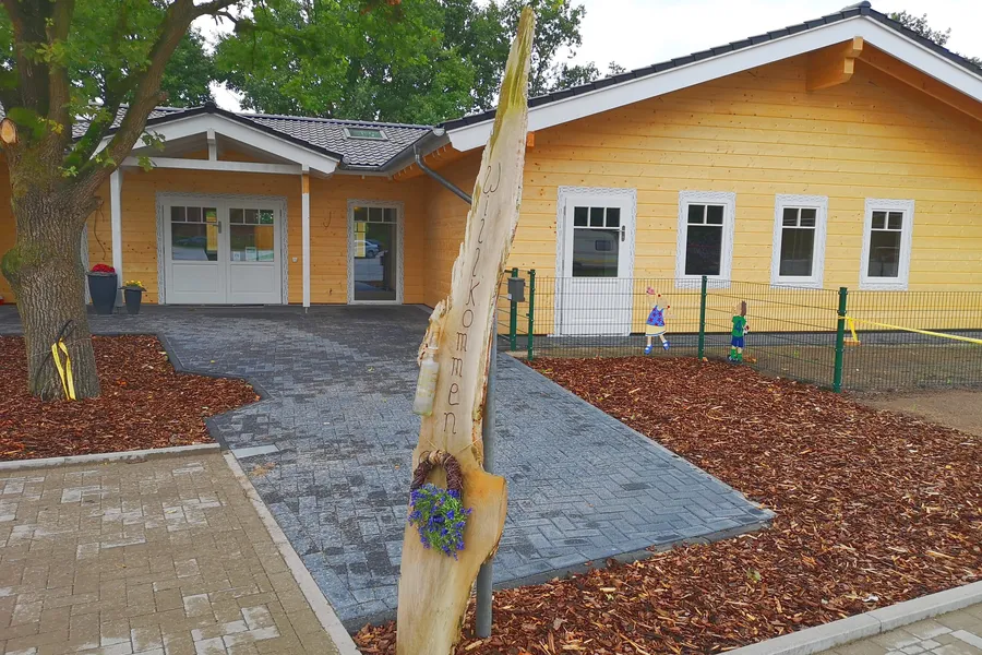 Der gelbe Holzbau der DRK-Kita mit Vordach und gepflastertem Zugang
