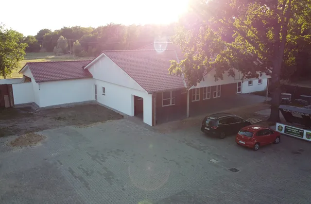Das Dorfgemeinschaftshaus, ein weiß-rotes Gebäude mit Parkplatz davor, im Gegenlicht der tiefstehenden Sonne